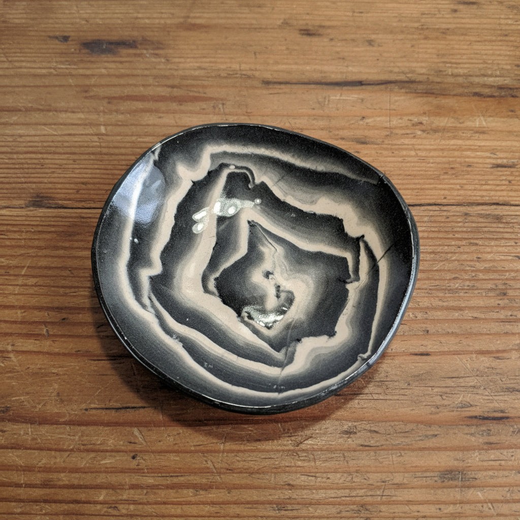 Round ceramic plate with black and white concentric pattern on a light gray background